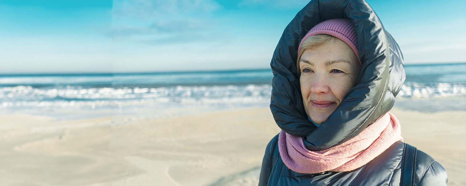 Goed ingeduffelde denkende vrouw aan de Noordzee als illustratie voor de vergelijkingspagina van pensioenproducten van DVV 