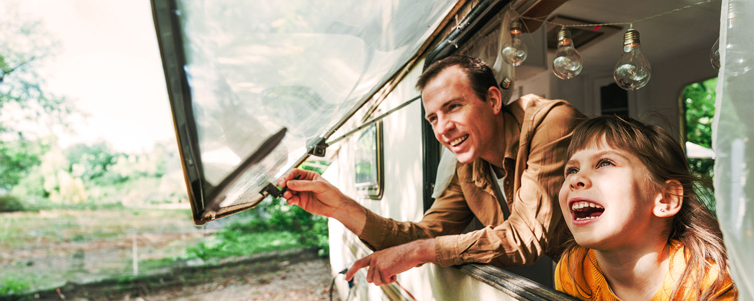 Un père et sa fille regardent par la fenêtre du camping-car pour illustrer la page de l'assurance camping-car de la DVV 