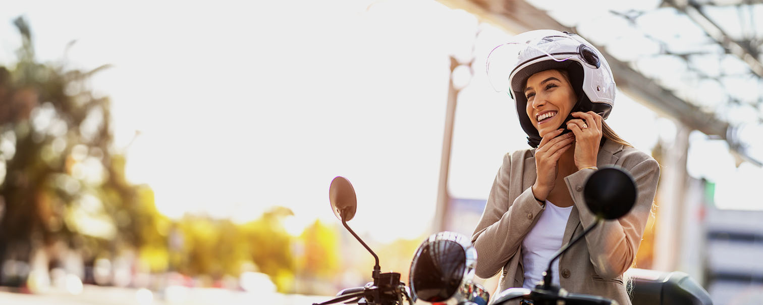 Vrouw op een scooter die  helm aandoet als illustratie voor de pagina van de moto- en scooterverzekeringen van DVV 