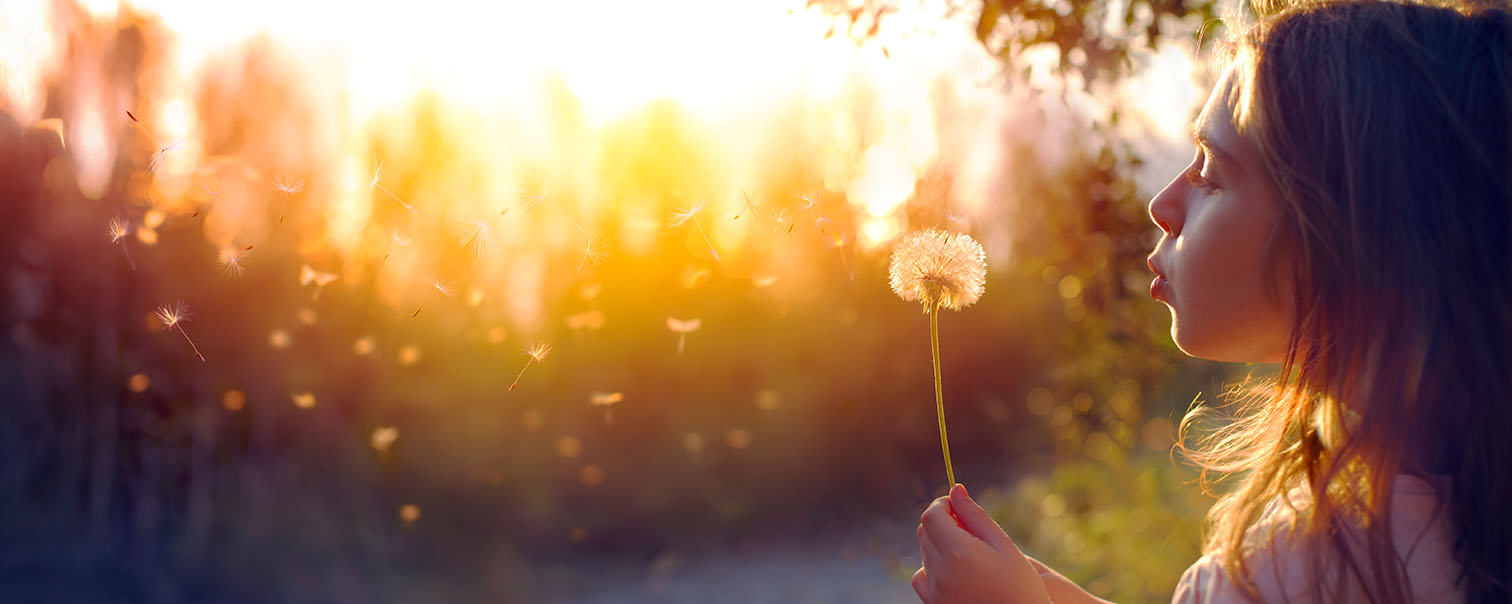 Vrouw die op een zonnebloem blaast en de deeltjes vliegen richting hemel als illustratie voor de pagina overlijdensverzekering van DVV 