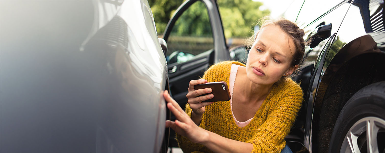 Jeune femmme inspectant deux voitures après un accident pour illustrer la page comparative de protection juridique auto