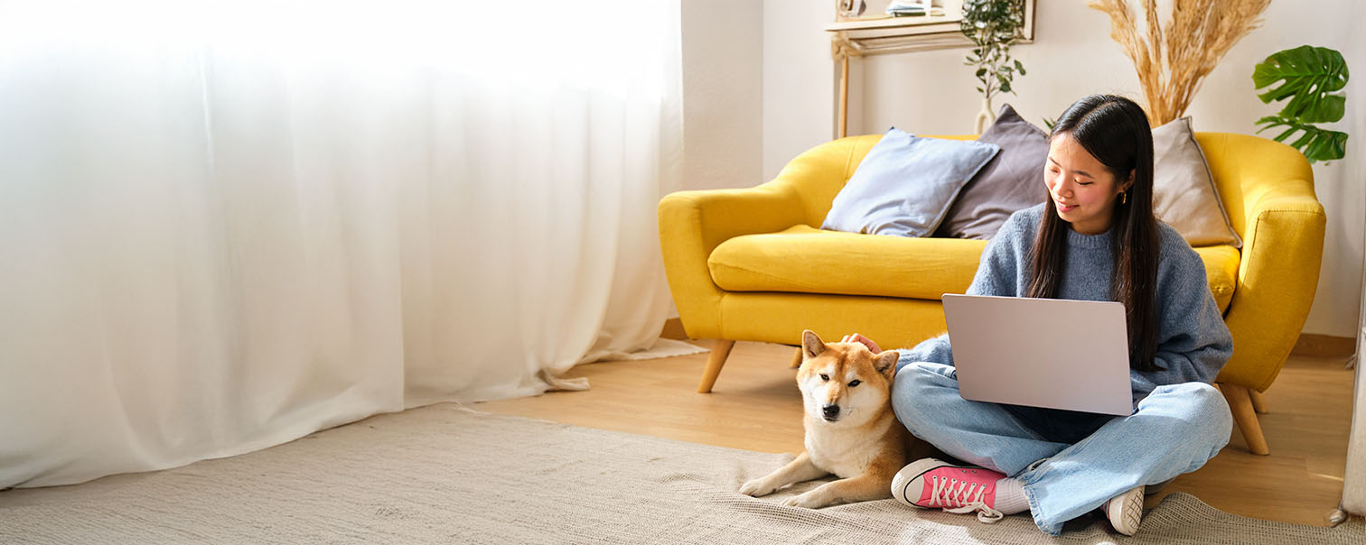 Jeune femme assise par terre devant son canapé avec son portable pour illustrer l'Option Media de l'assurance habitation