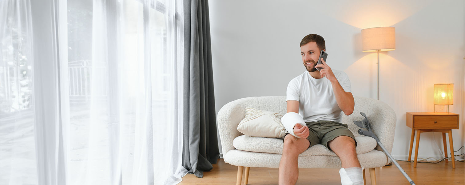 Un travailleur indépendant, dans son fauteuil, plâtré, en train d’appeler son conseiller DVV pour déclarer un sinistre lié au monde du travail. 