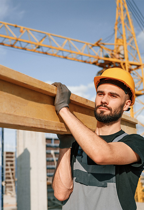 Personne portant une poutrelle en bois pour illustrer la page de l'assurance Accidents du travail de DVV